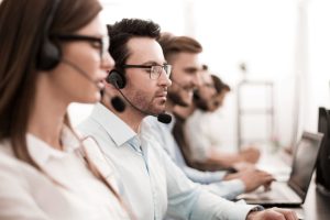 Close up of people in front of computers with headsets.