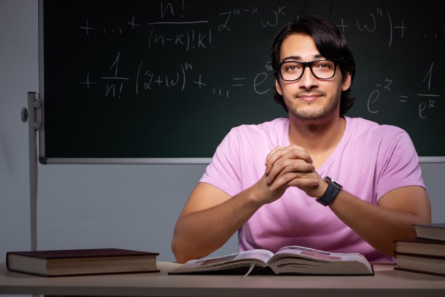 Male student sitting in classroom post img Male student sitting in classroom with blackboard behind him.