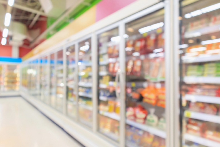 Supermarket aisle with commercial refrigerators freezer showing frozen foods abstract blur background.