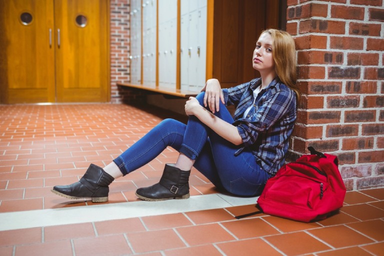Worried student sitting on the floor post img Worried student sitting on the floor against brick wall in school hallway